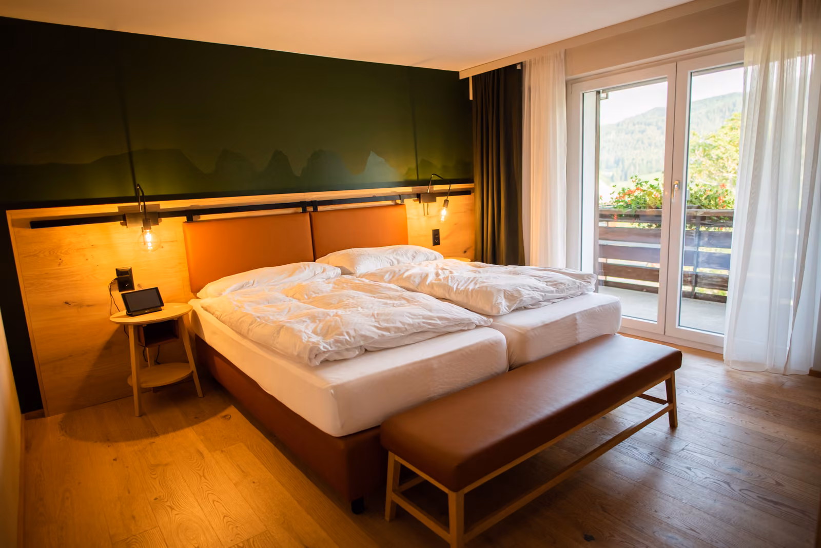 Zimmer mit Holzboden, Doppelbett, Lederbank und Balkontür